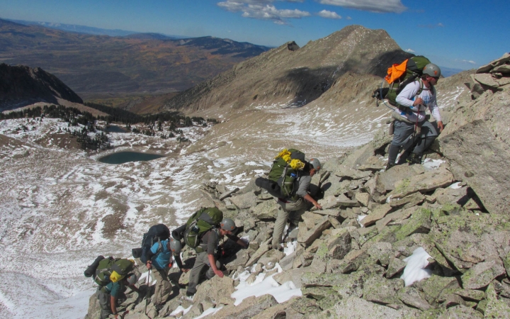A group of people wearing safety gear make their way up a rocky landscape.